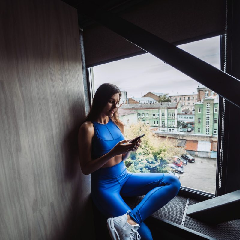 Pretty girl sitting on the window sill with smartphone in hands. Pretty girl sitting on the window sill with smartphone in hands.